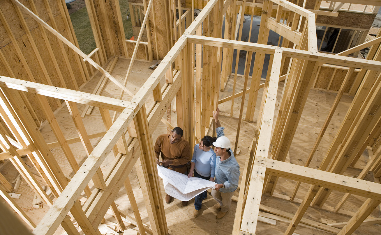 Three adults looking at building plans while standing in a house under construction.