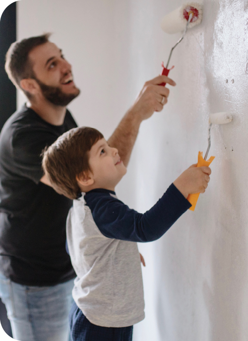 A father and son roll white paint on a wall.