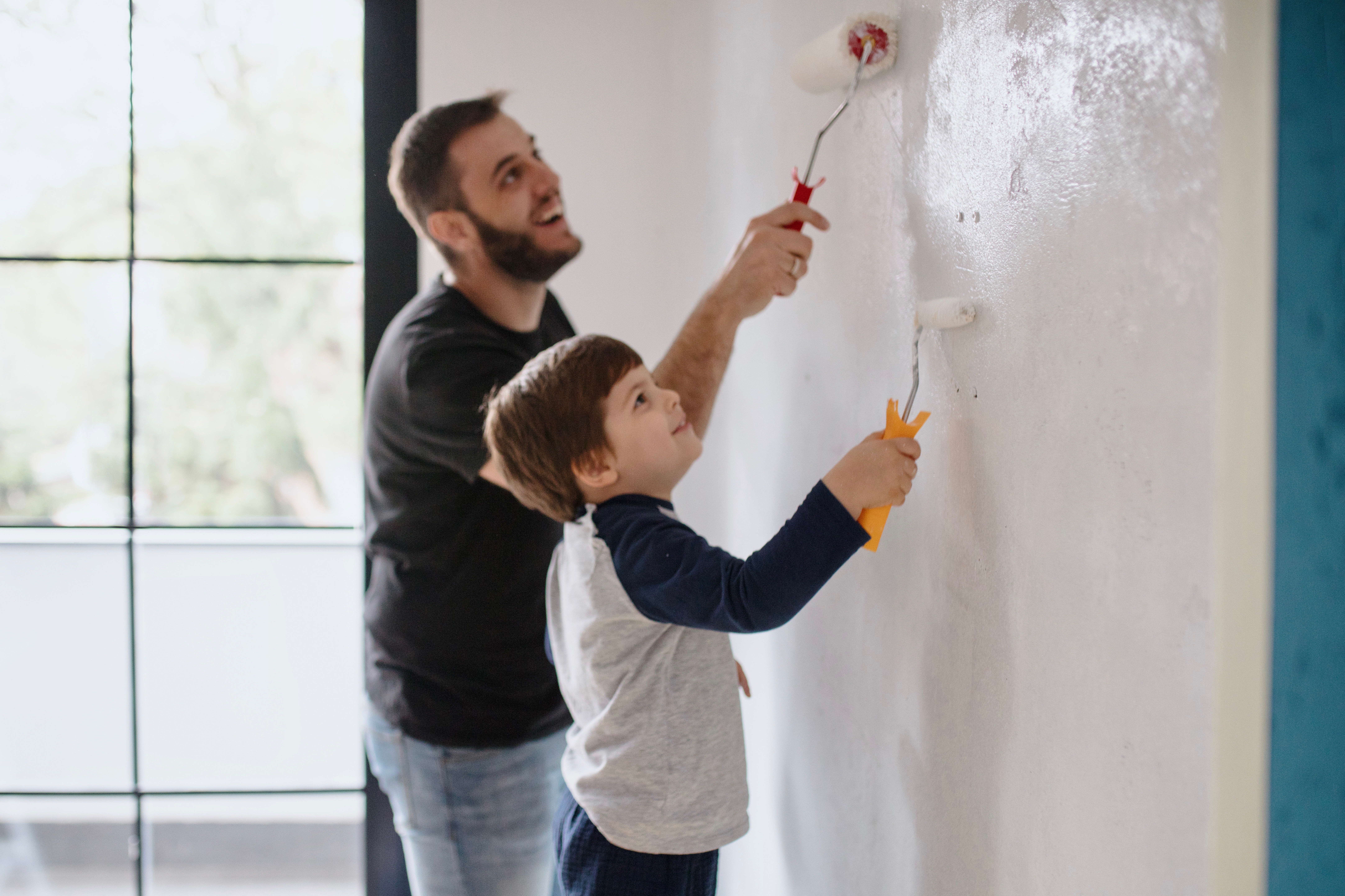A father and son roll white paint on a wall.