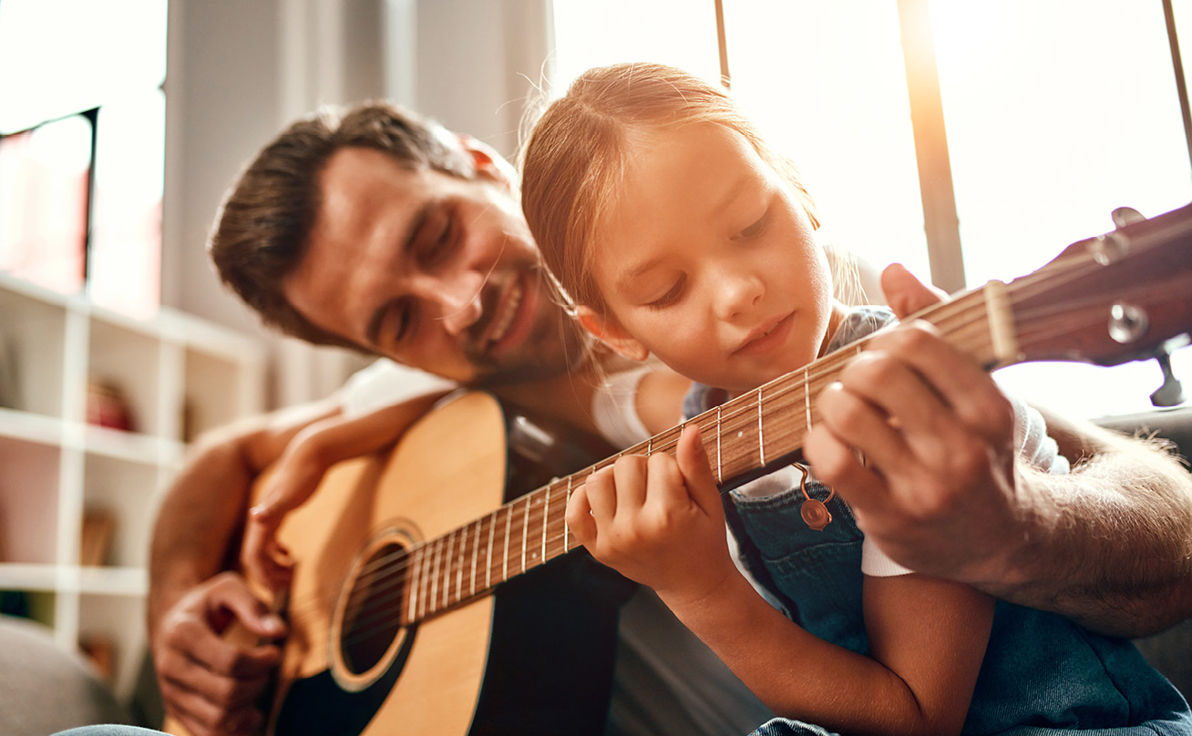 A father teaching his young daughter how to play guitar.