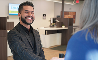 A male employee with a beard is smiling and shaking hands with a member.