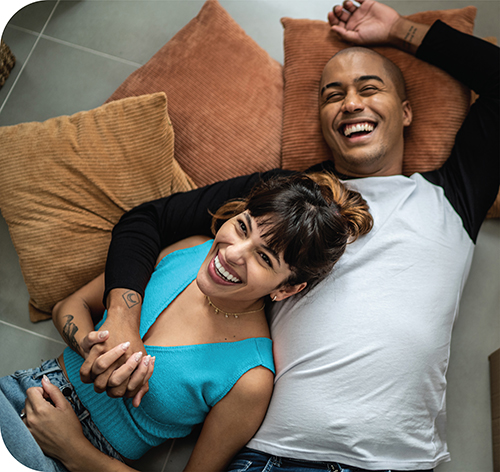 A couple, who is laughing and laying on the floor in their first home.