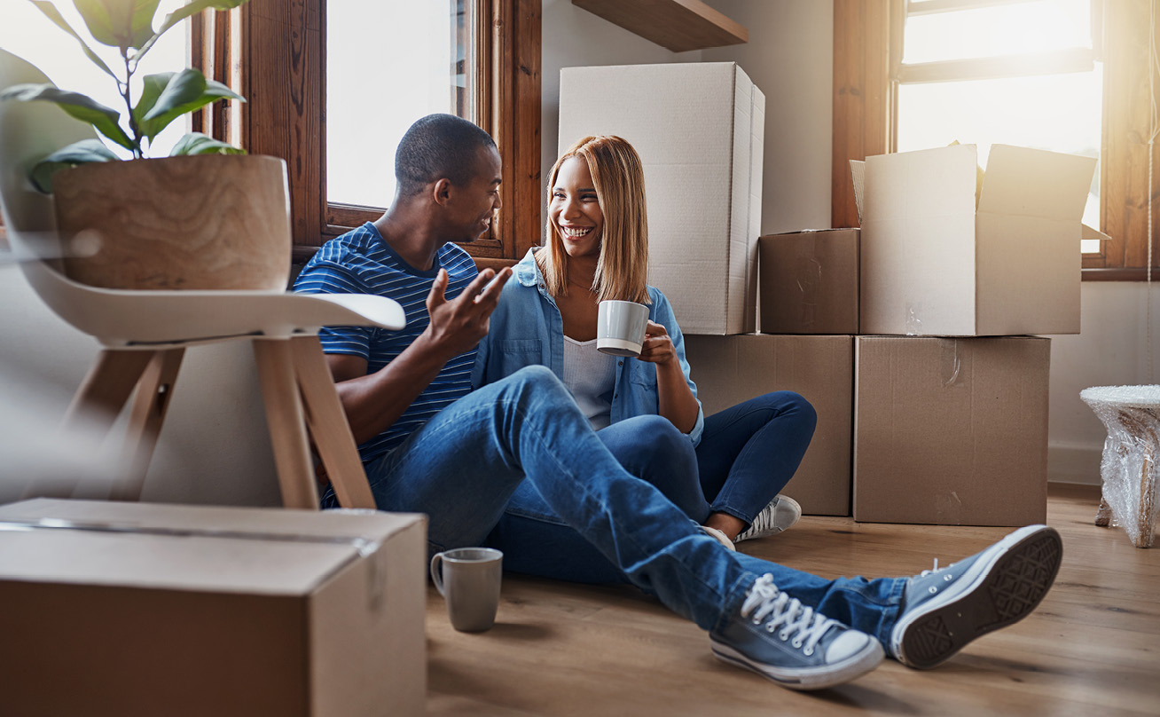 A young, black couple drink coffee on the floor of their new home.