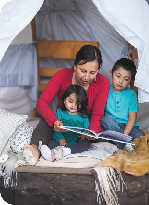 An Indigenous woman reads a book to her two young children.