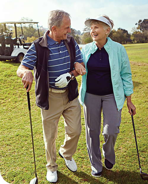 A senior couple hold golf clubs and smile at each other on a sunny U.S. golf course. 