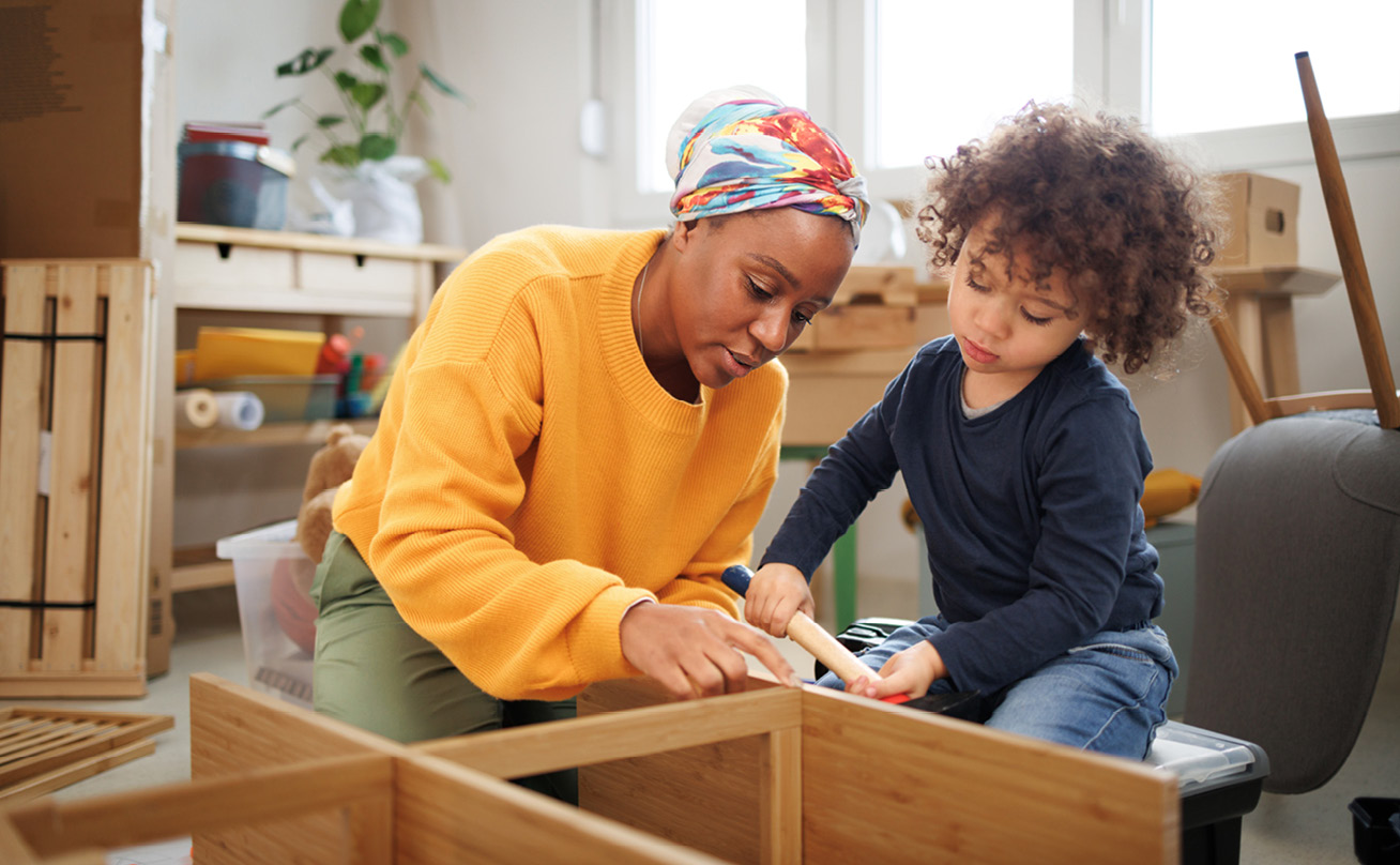 A black mother and her young son build a bookshelf together.
