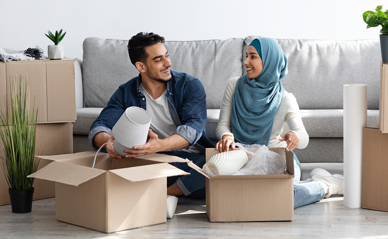 A young Muslim couple unpack moving boxes in their new living room.