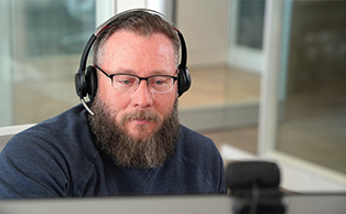  A male employee with a beard is wearing glasses and a headset. 